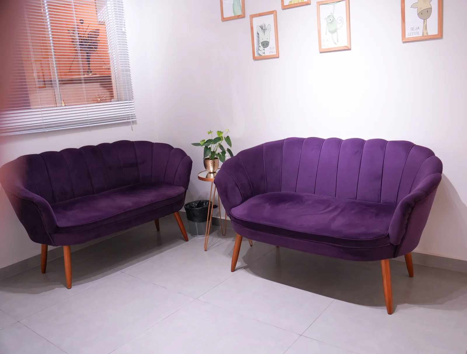 Dois sofás de veludo roxo em sala de espera clara, com quadros e planta
