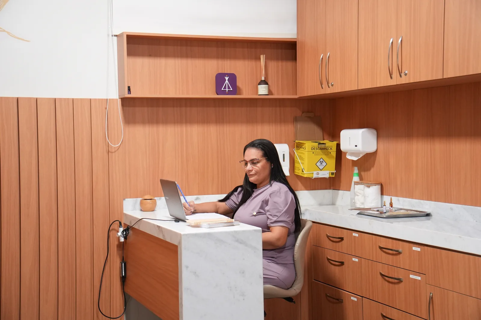 Enfermeira na estação de trabalho da sala, registrando o atendimento no computador