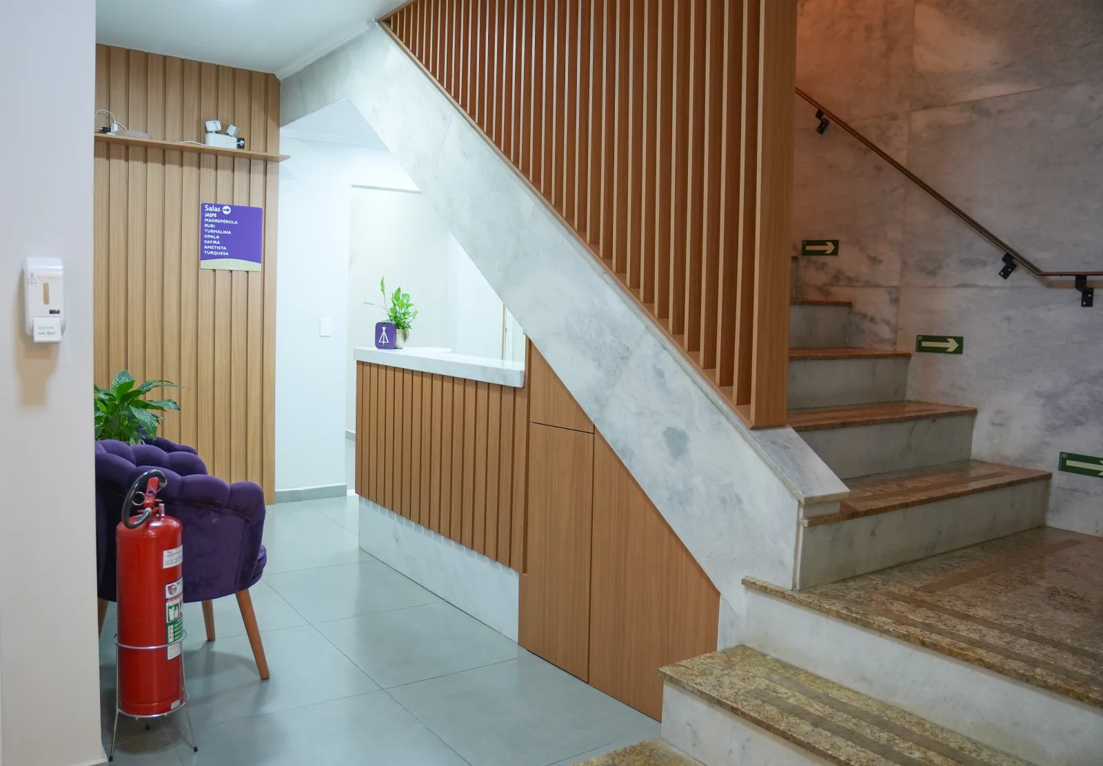 Hall de entrada da clínica com escada de mármore e parede ripada de madeira