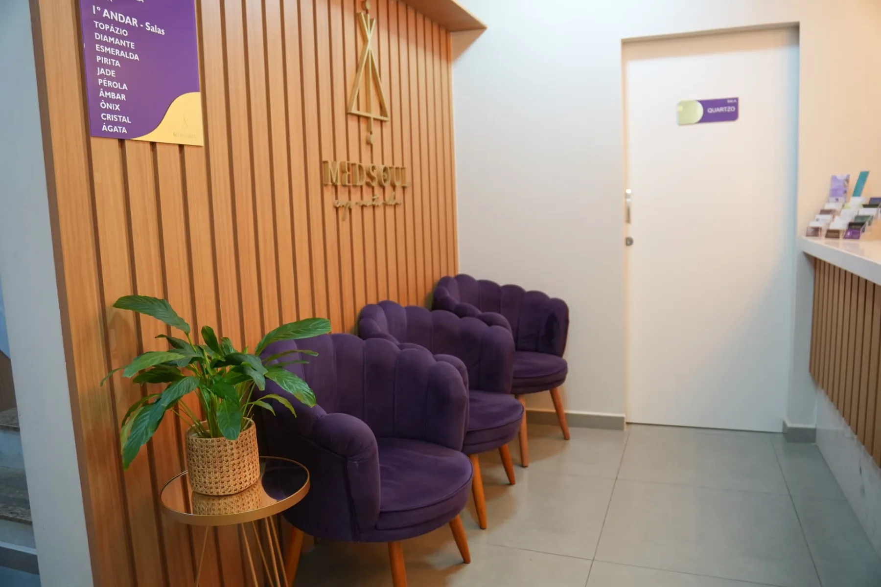 Recepção da MedSoul com poltronas de veludo roxo e parede ripada de madeira