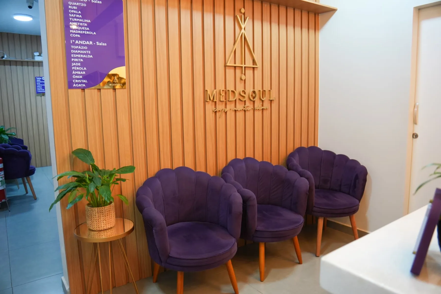 Área de espera da MedSoul com poltronas de veludo roxo e logo dourado na parede ripada